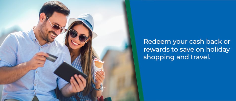 Redeem your cash back rewards to save on holiday shopping and travel - Image of a man and woman outside wearing sunglass holding a credit card and looking at a mobile phone